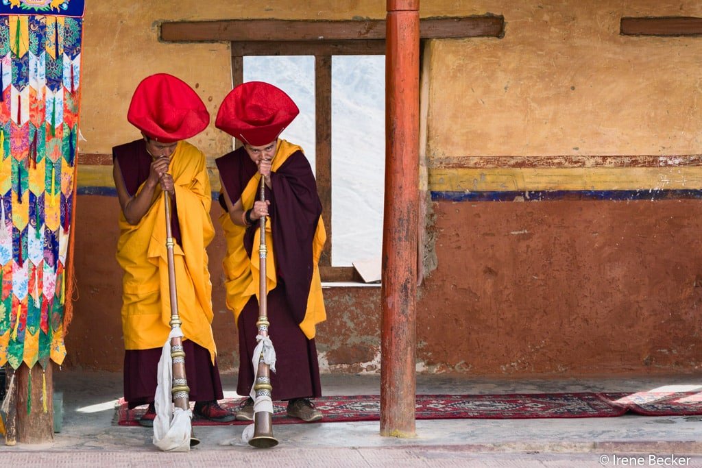 Two monks in red hats playing long horns during a ceremony in Leh