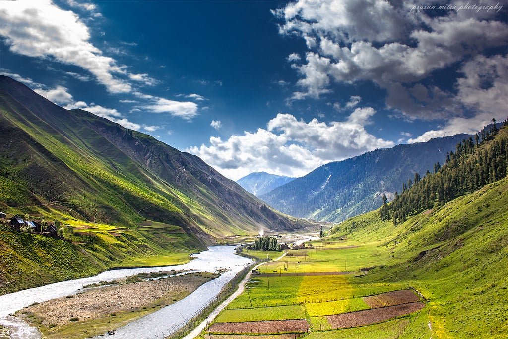 River winding through lush green valley with farmlands, mountains, and scattered homes