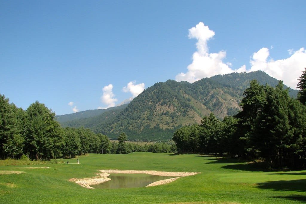 A golf course surrounded by pine trees and mountains under a blue sky