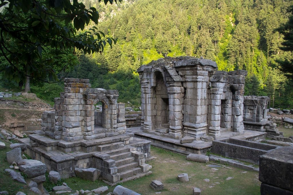 Ancient stone ruins of the historic Pandrethan Temple set against a dense forest backdrop in Kashmir
