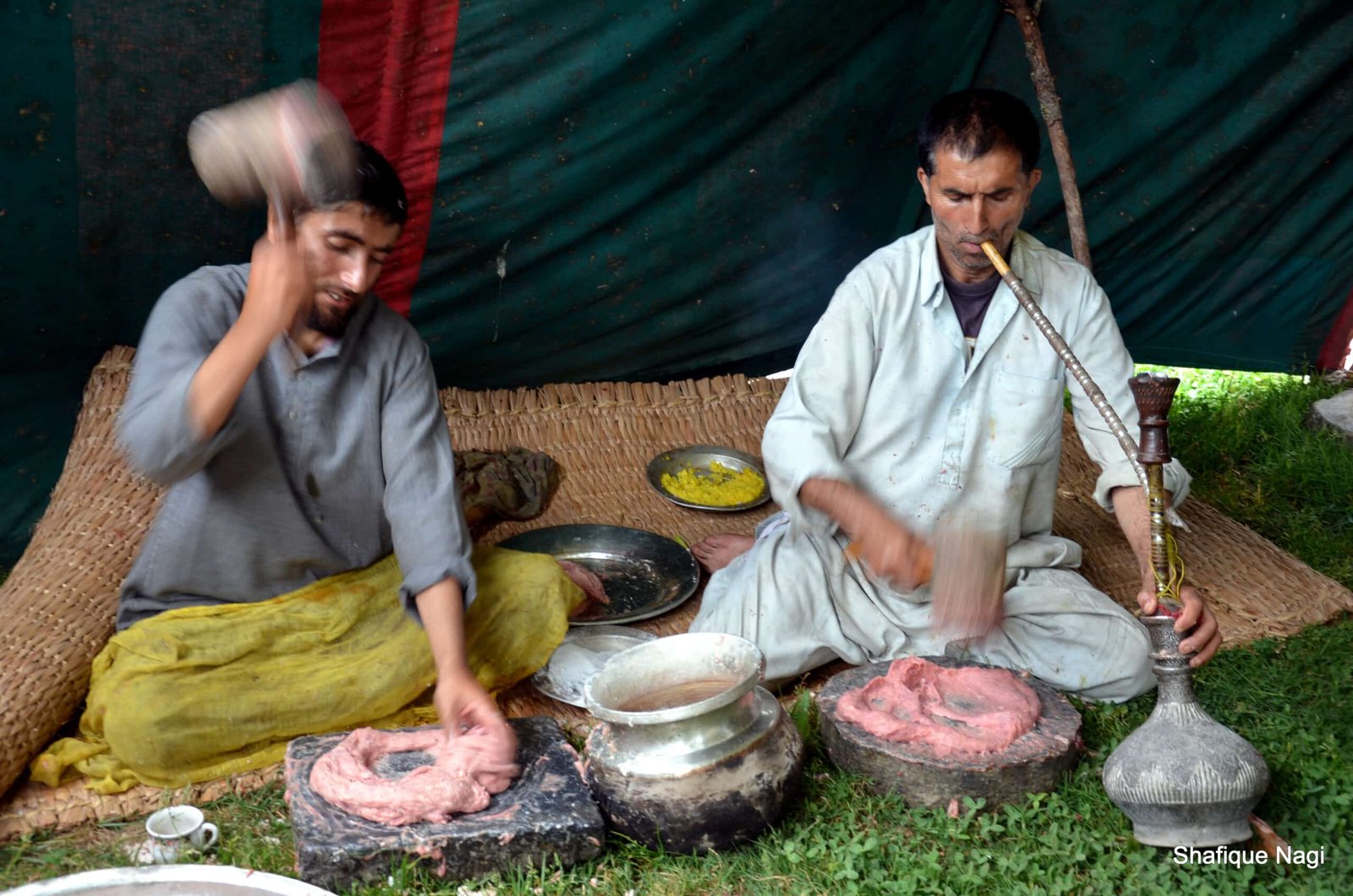 Two Kashmiri men preparing traditional meat dish using wooden mallets