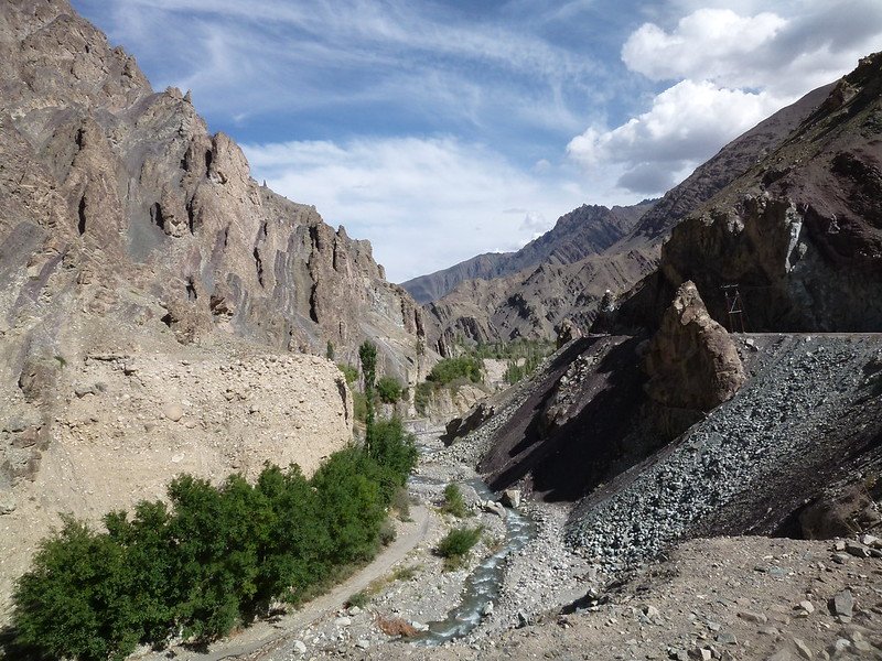 Narrow rocky valley with a stream and green trees surrounded by barren mountains in Sham Valley, ladakh
