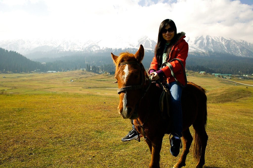 Woman riding a horse in a mountain meadow with snowy peaks in baisaran valley