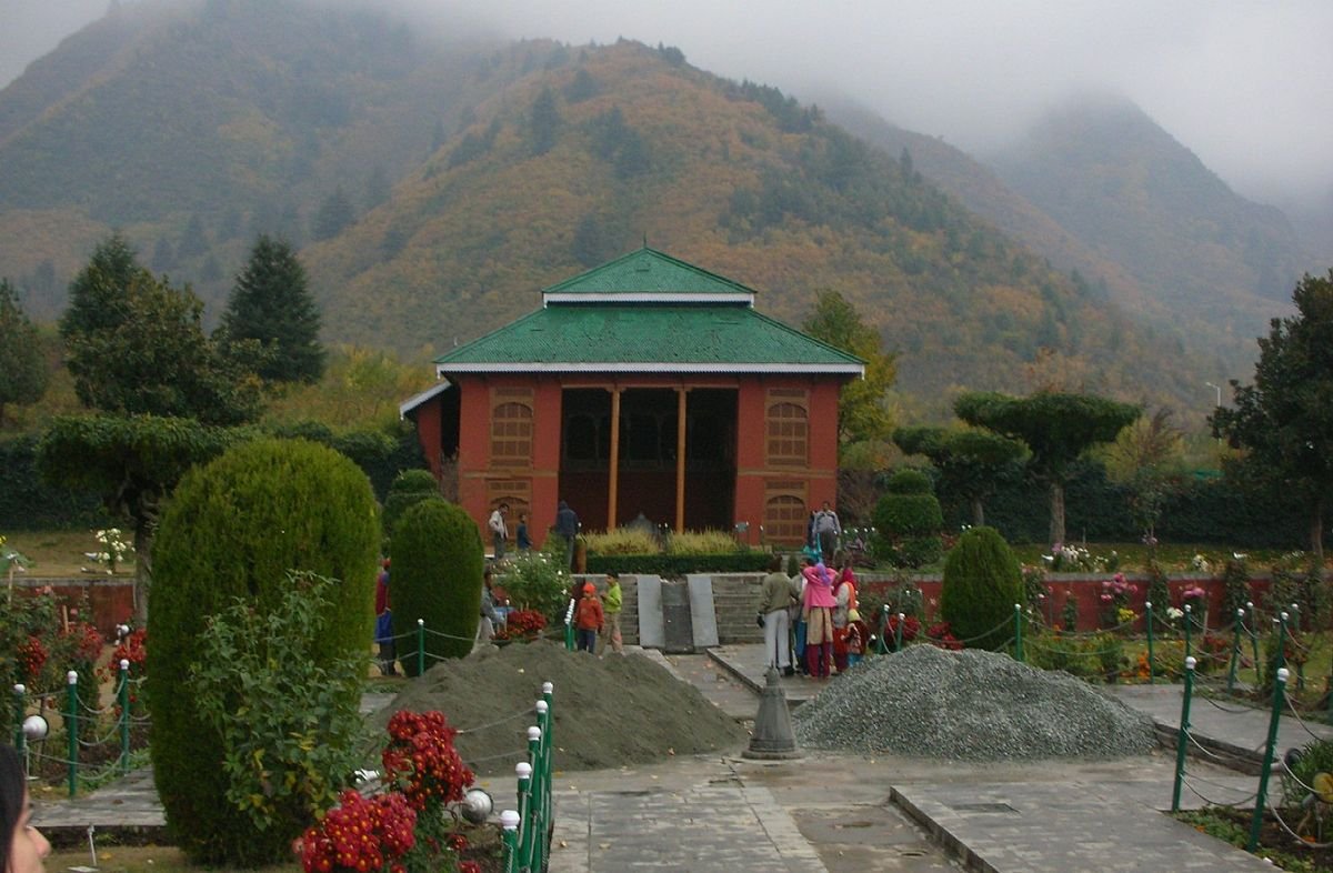 People walking in a garden with a pavilion and misty mountains in the background