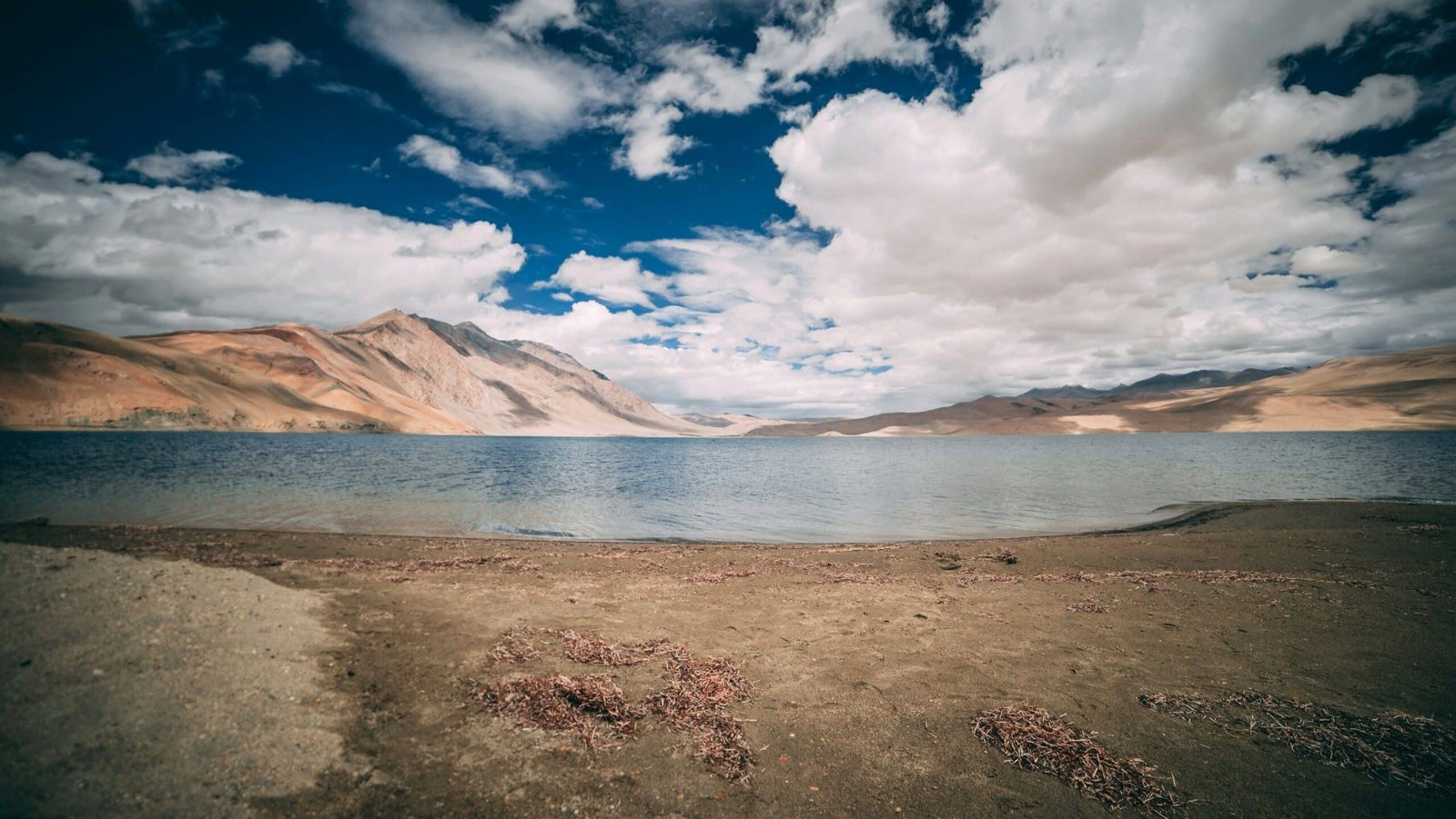 Arid mountains and cloudy sky reflected in the calm waters of Tso Kar Lake in Ladakh