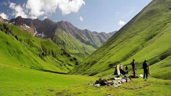 People standing on lush green meadows surrounded by steep hills at Doodhpathri