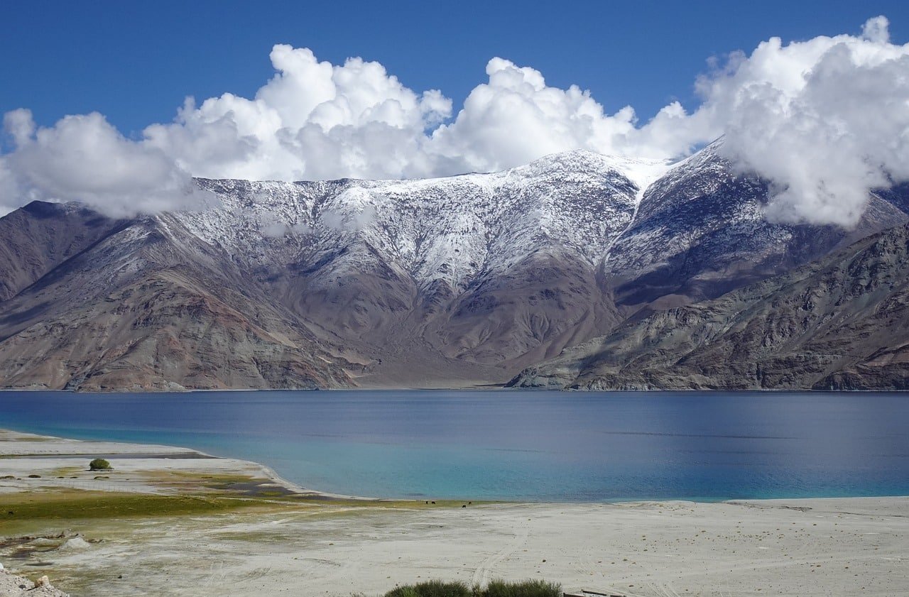 Scenic view of Pangong Lake with snow-covered mountains and dramatic clouds