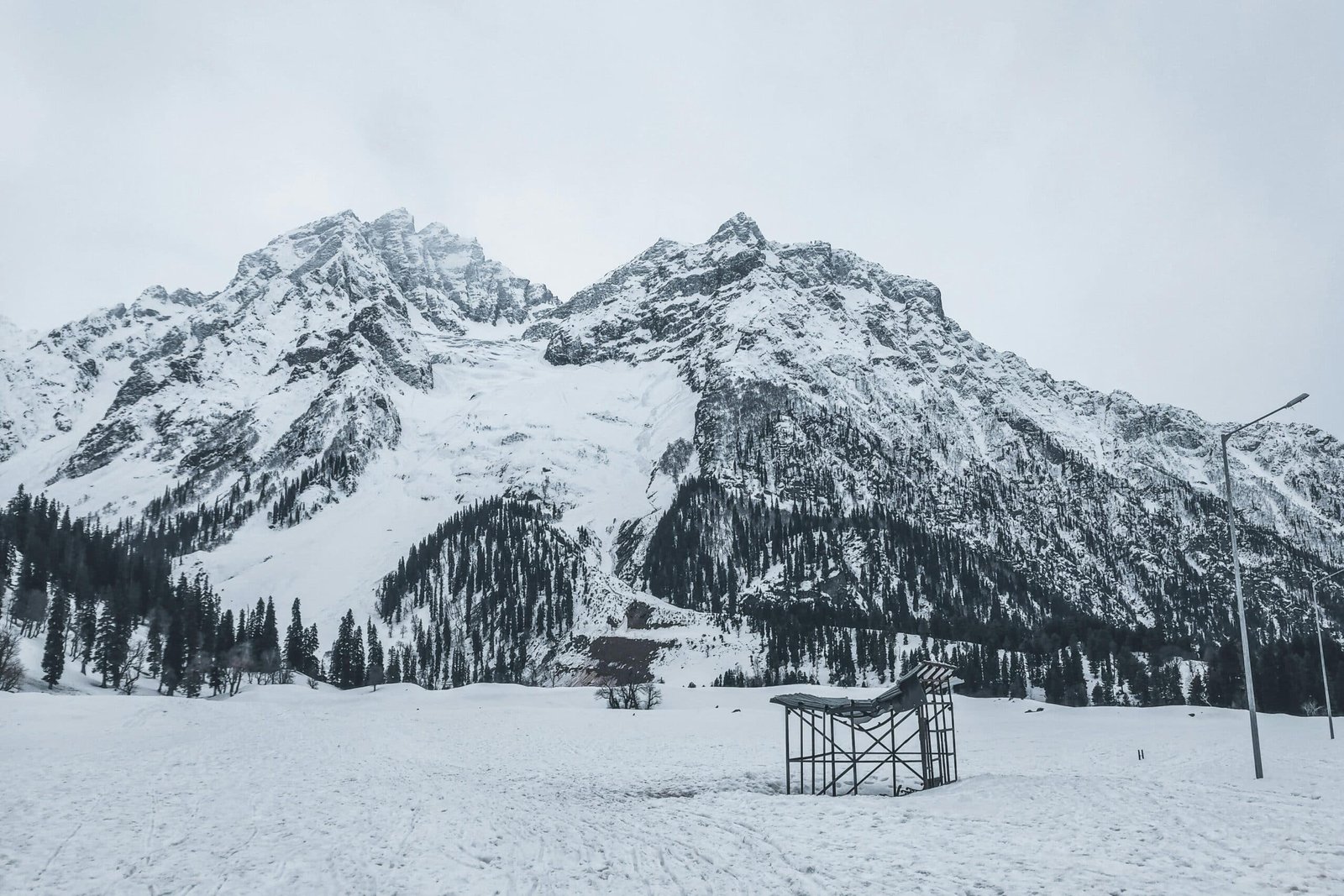 Snow-covered mountains with pine trees and a broken shelter structure during winter in kashmir