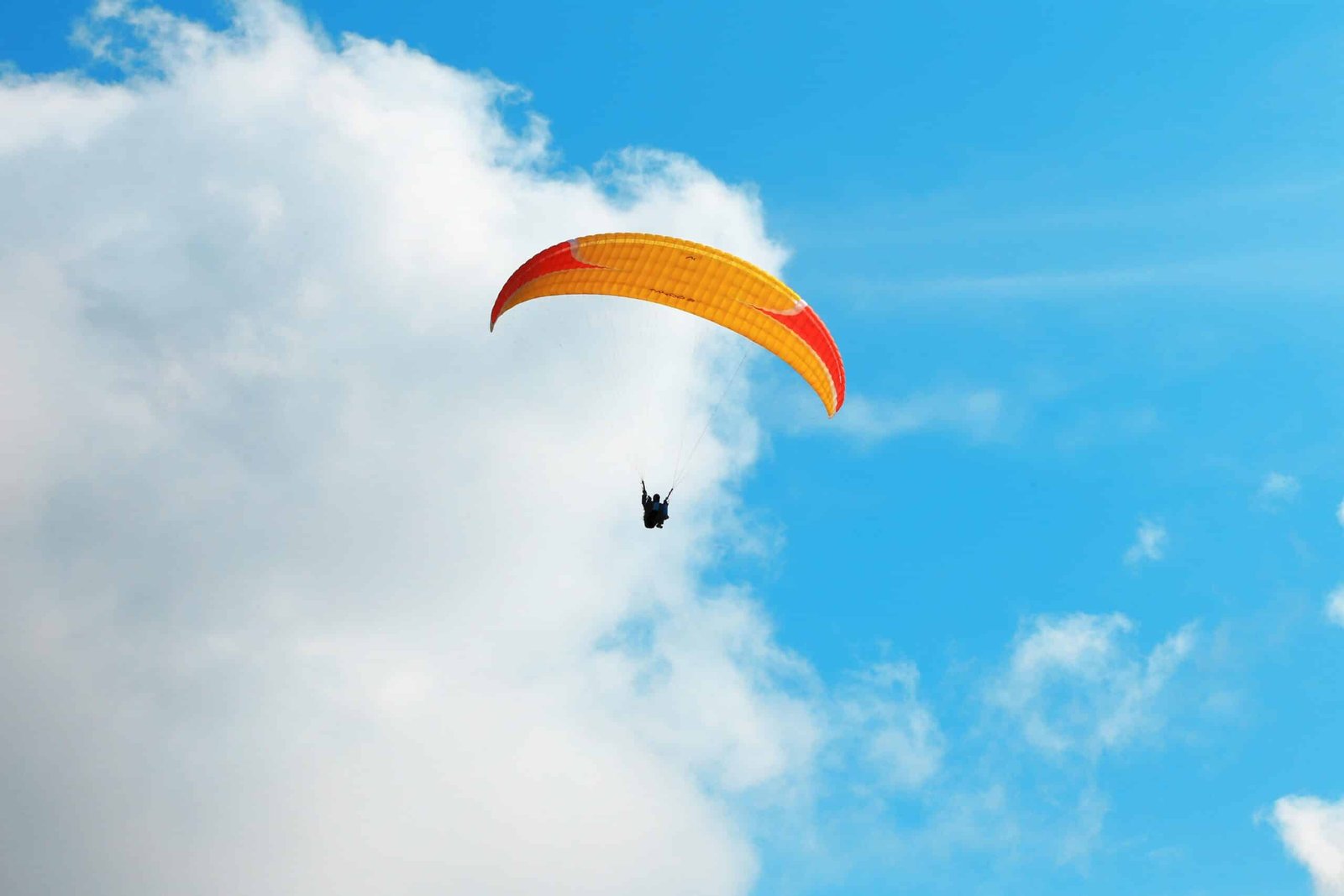 Person paragliding with an orange and red parachute against a bright blue sky in srinagar