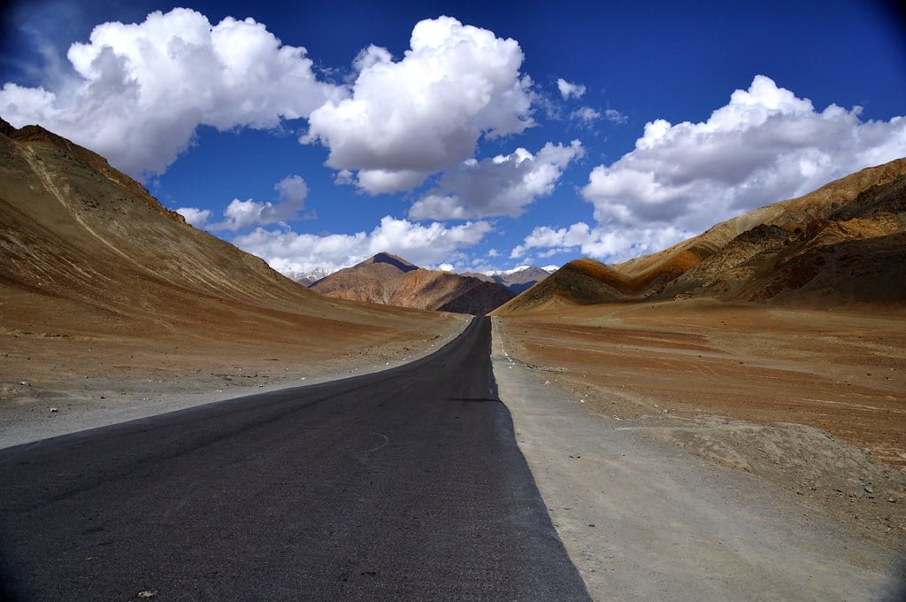 Empty road through brown mountains under a blue sky at Magnetic Hill, Ladakh