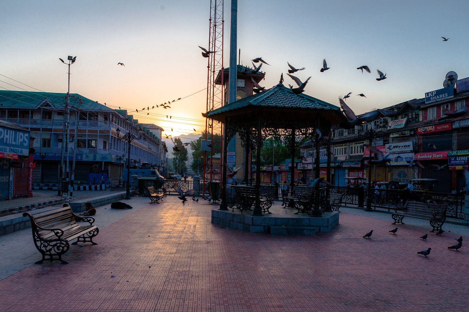 Empty Lal chowk in Srinagar at sunrise with benches, birds, and buildings