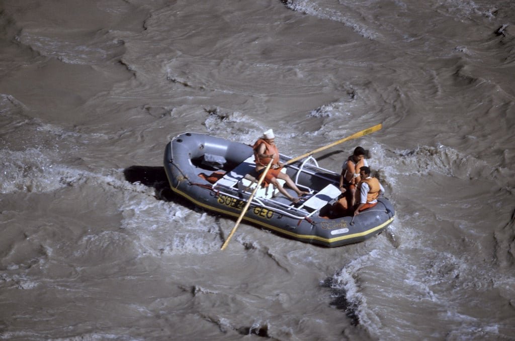 People rafting through the rapids of the Zanskar River in a grey inflatable boat wearing life jackets