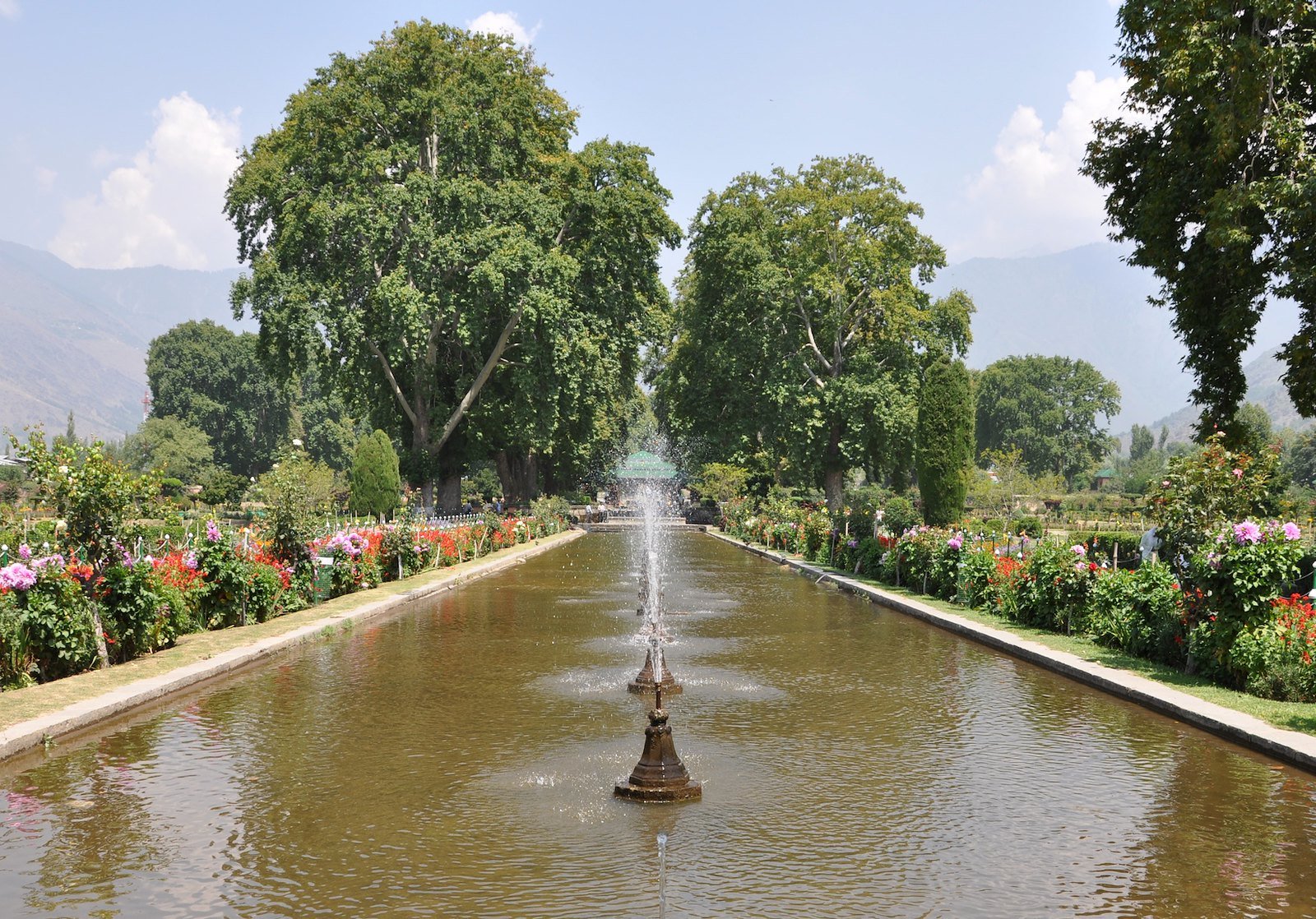 Water fountain in a garden walkway at Shalimar Bagh with trees and flowers
