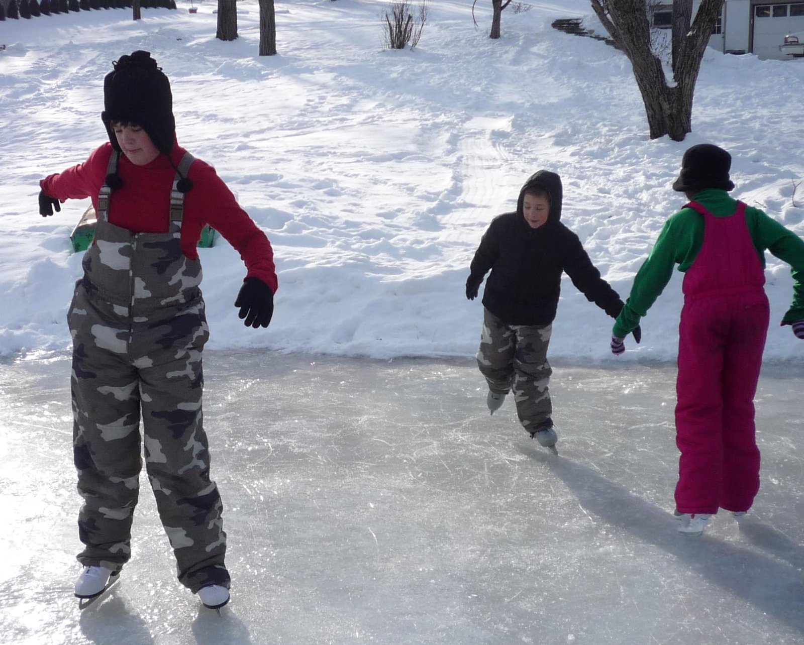 Three children ice skating on an outdoor frozen surface.