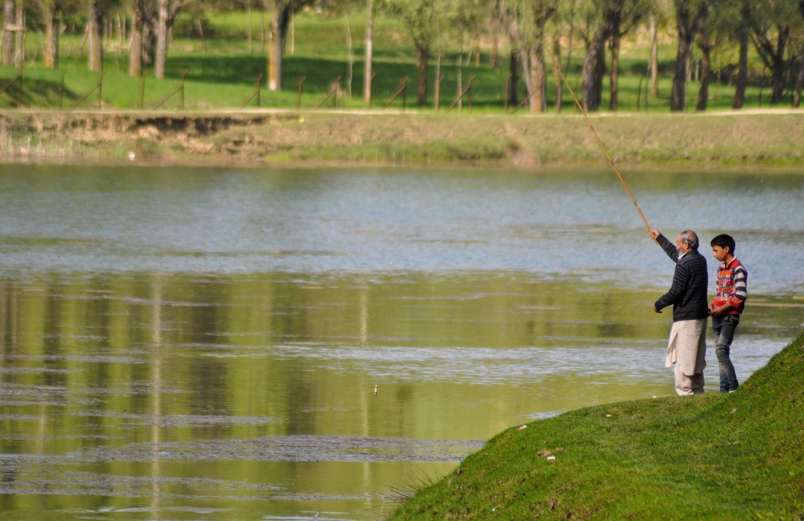 Two people fishing by the shore of Nilnag Lake surrounded by greenery