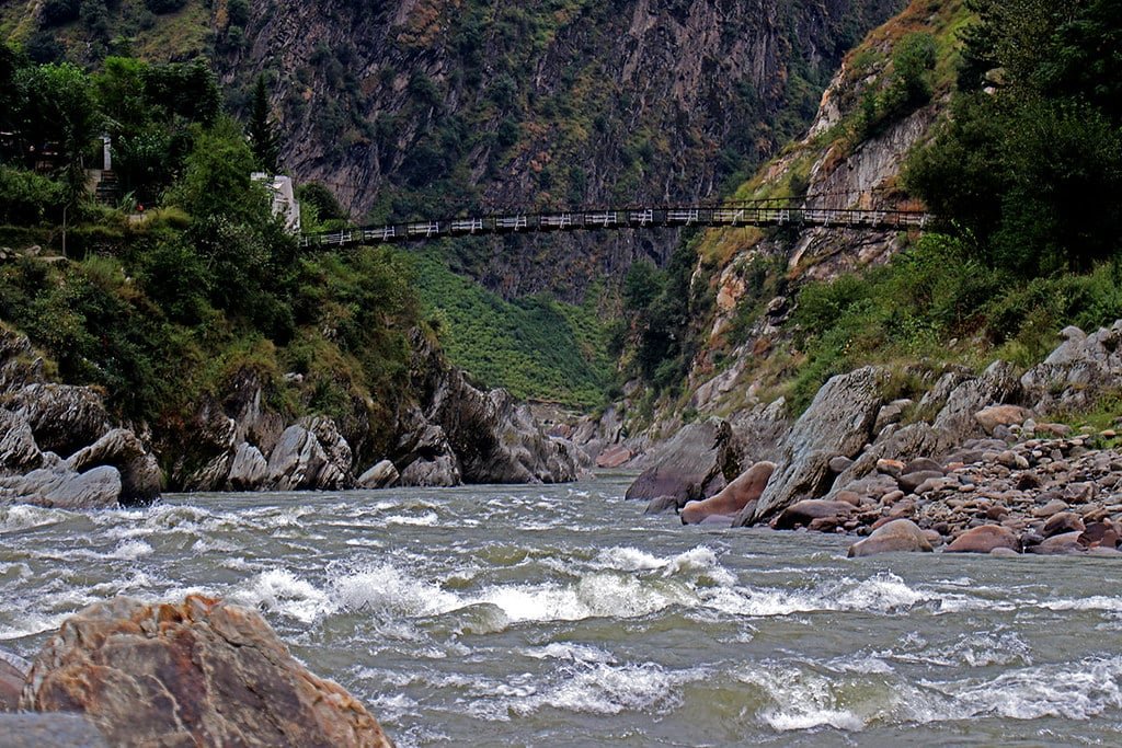 Rushing river with a hanging bridge and rocky cliffs on both sides at Teetwal Valley