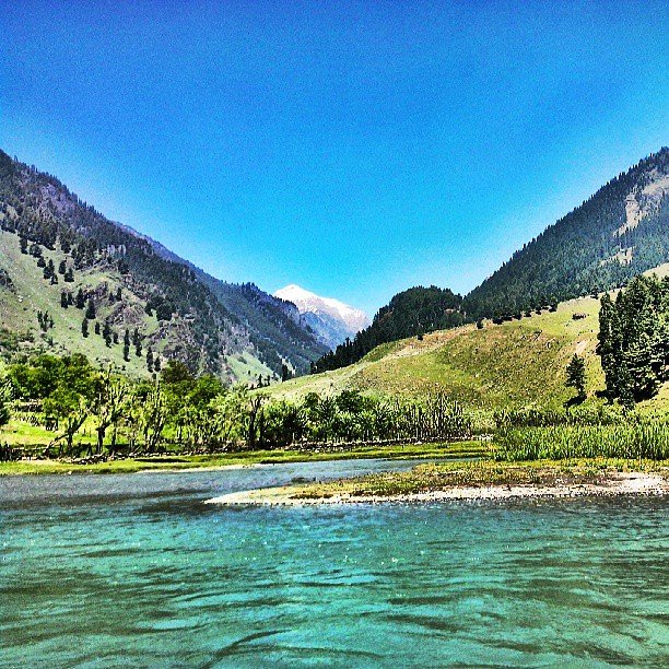 Clear blue river flowing through a lush green valley with forested mountains
