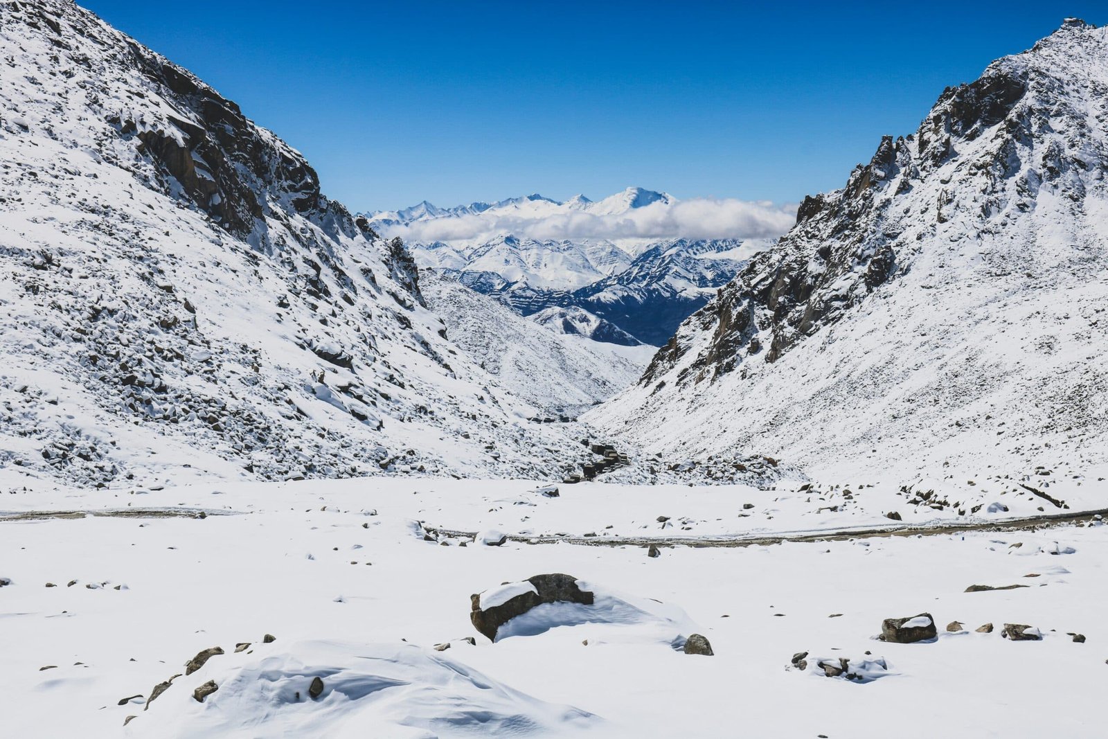 Snow-covered mountain pass with distant peaks under a clear blue sky in ladakh