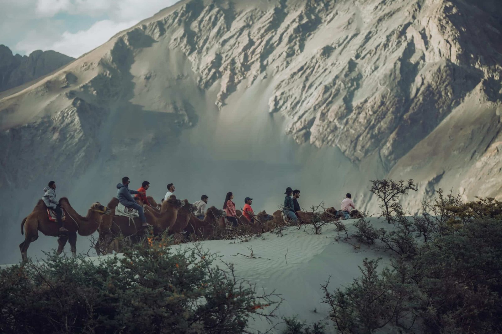 Tourists riding camels on sand dunes with mountains in the background