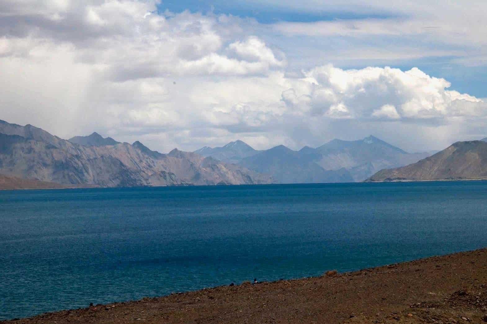 View of Pangong Lake with deep blue water, surrounded by rugged mountains under a partly cloudy sky
