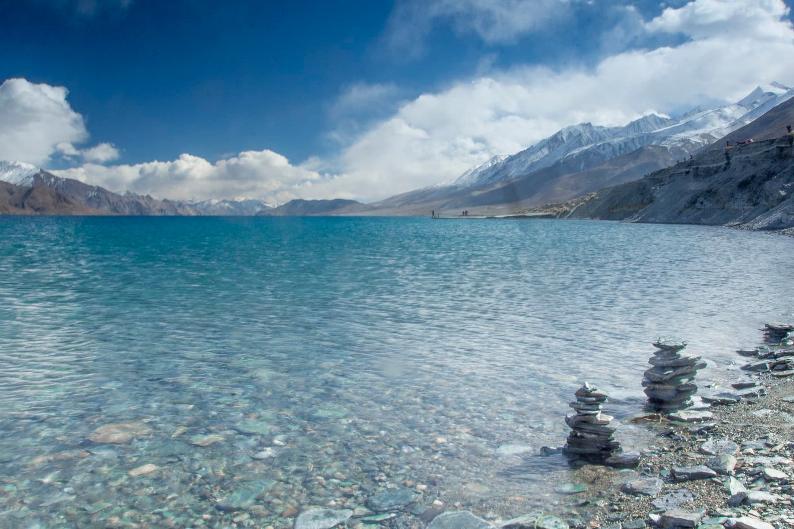 Stacked stones on the shore of Pangong Lake with clear turquoise water