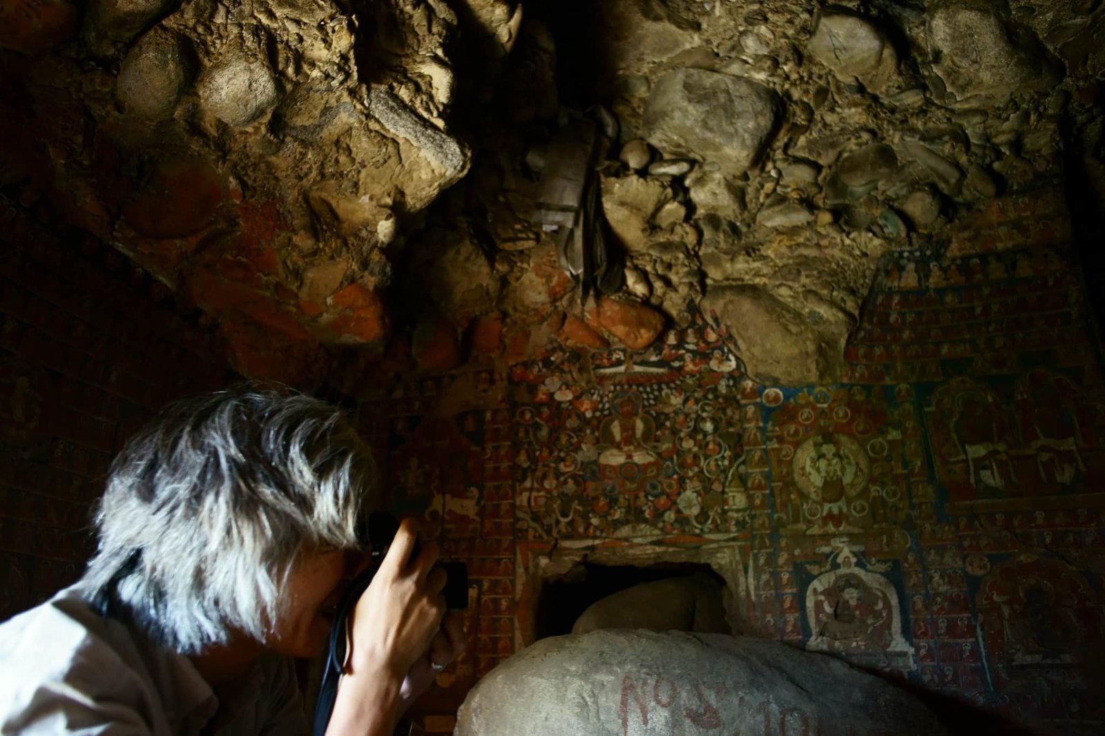Person photographing ancient Buddhist murals inside Saspol Caves in Ladakh