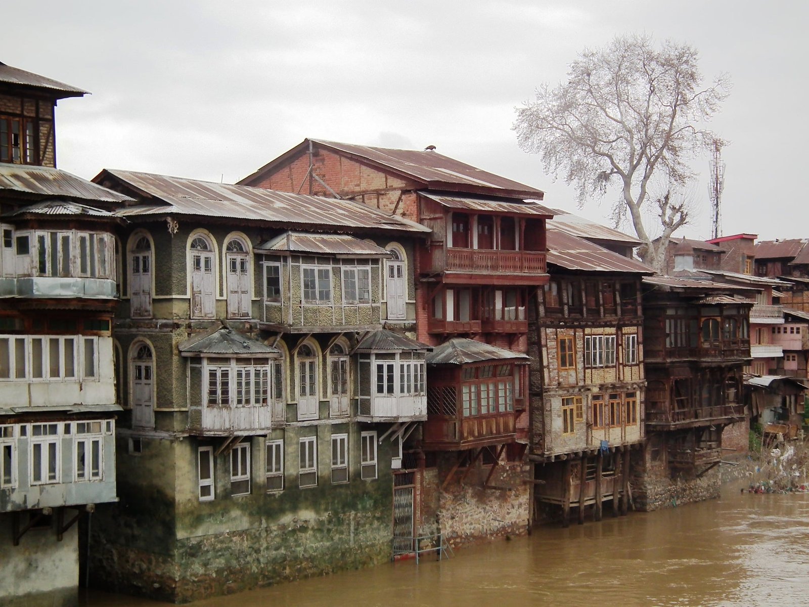 Old wooden houses with arched windows along the riverbank in Srinagar’s old city