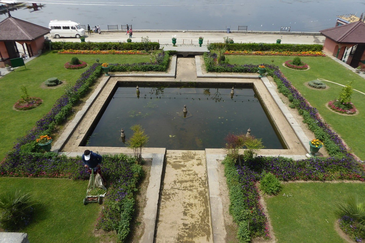 Man mowing lawn near a square pond in a nishant garden by the water