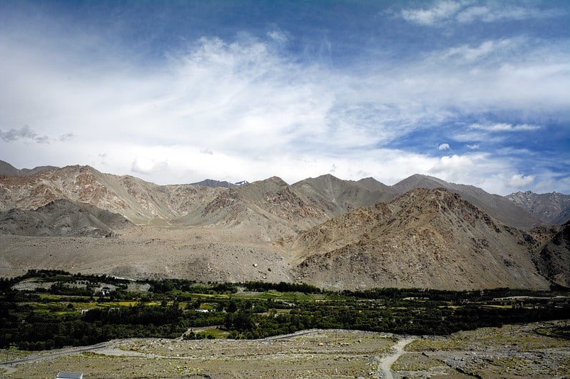 Mountain landscape at Khardung La Pass with scattered greenery below and blue sky above