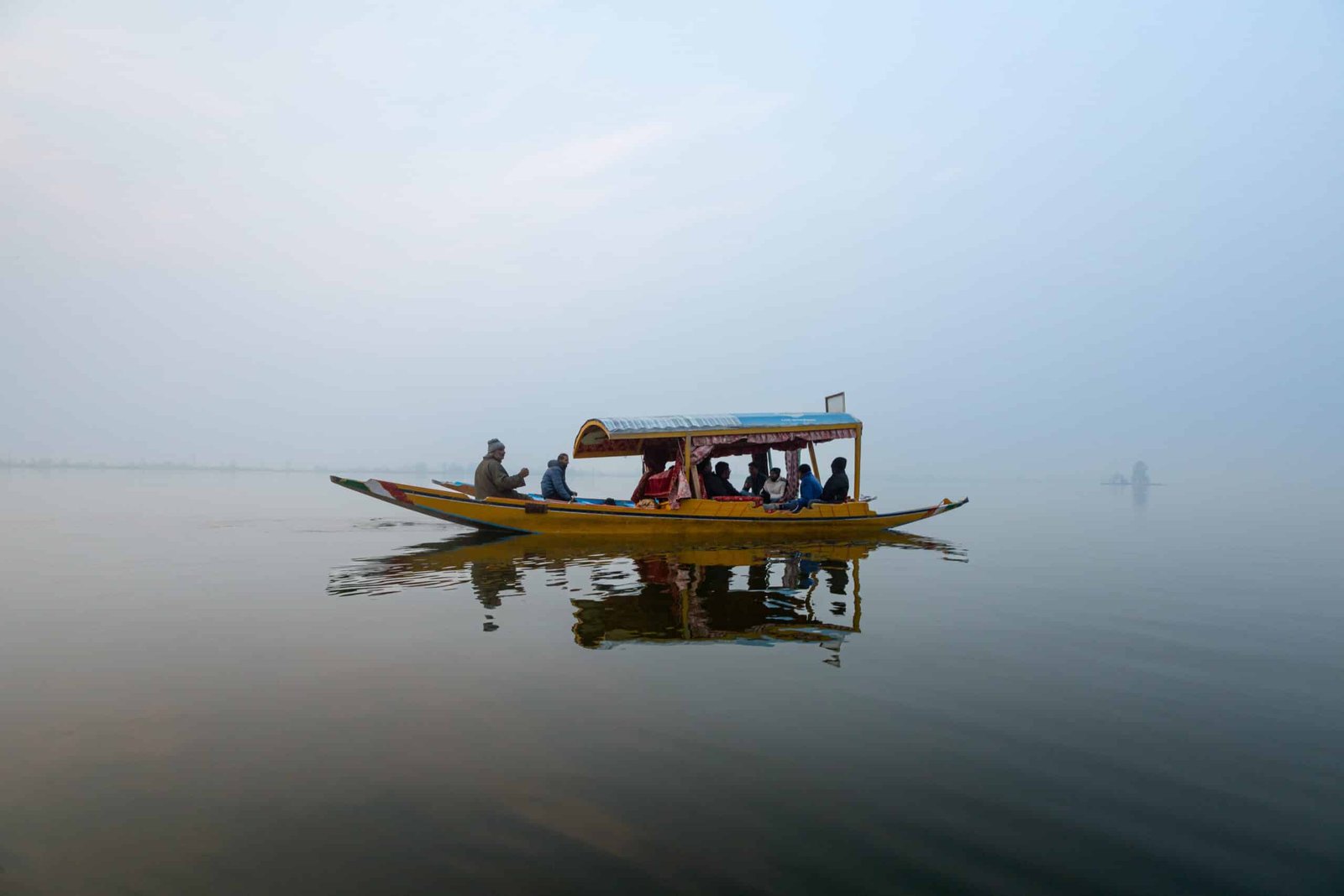 Traditional shikara boat carrying passengers glides over the calm waters of Dal Lake on a misty morning in Kashmir