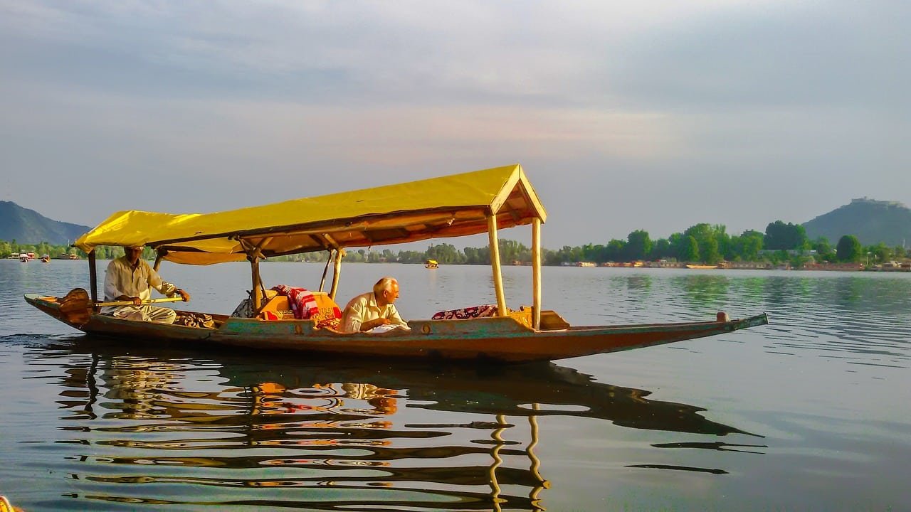 Two men on a traditional shikara boat with a yellow canopy on Dal Lake, Kashmir