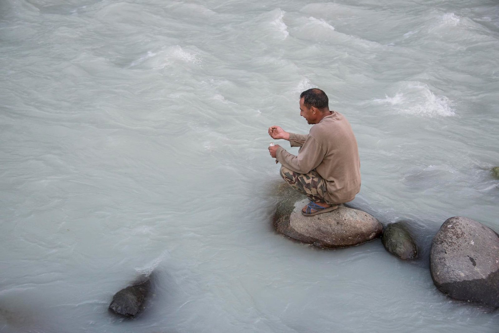 Man fishing in a river while sitting on a rock in pahalgam