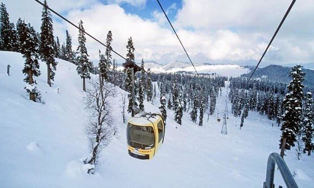 A yellow Gulmarg Gondola cabin gliding over snowy slopes