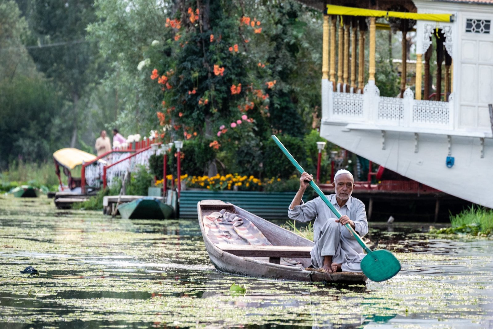 An elderly man paddles a wooden boat through a scenic waterway in Srinagar, Kashmir