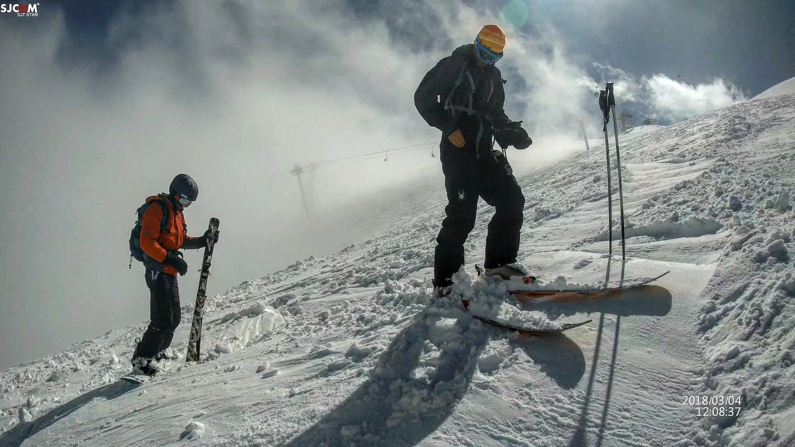 Two skiers on a snowy mountain slope preparing their gear