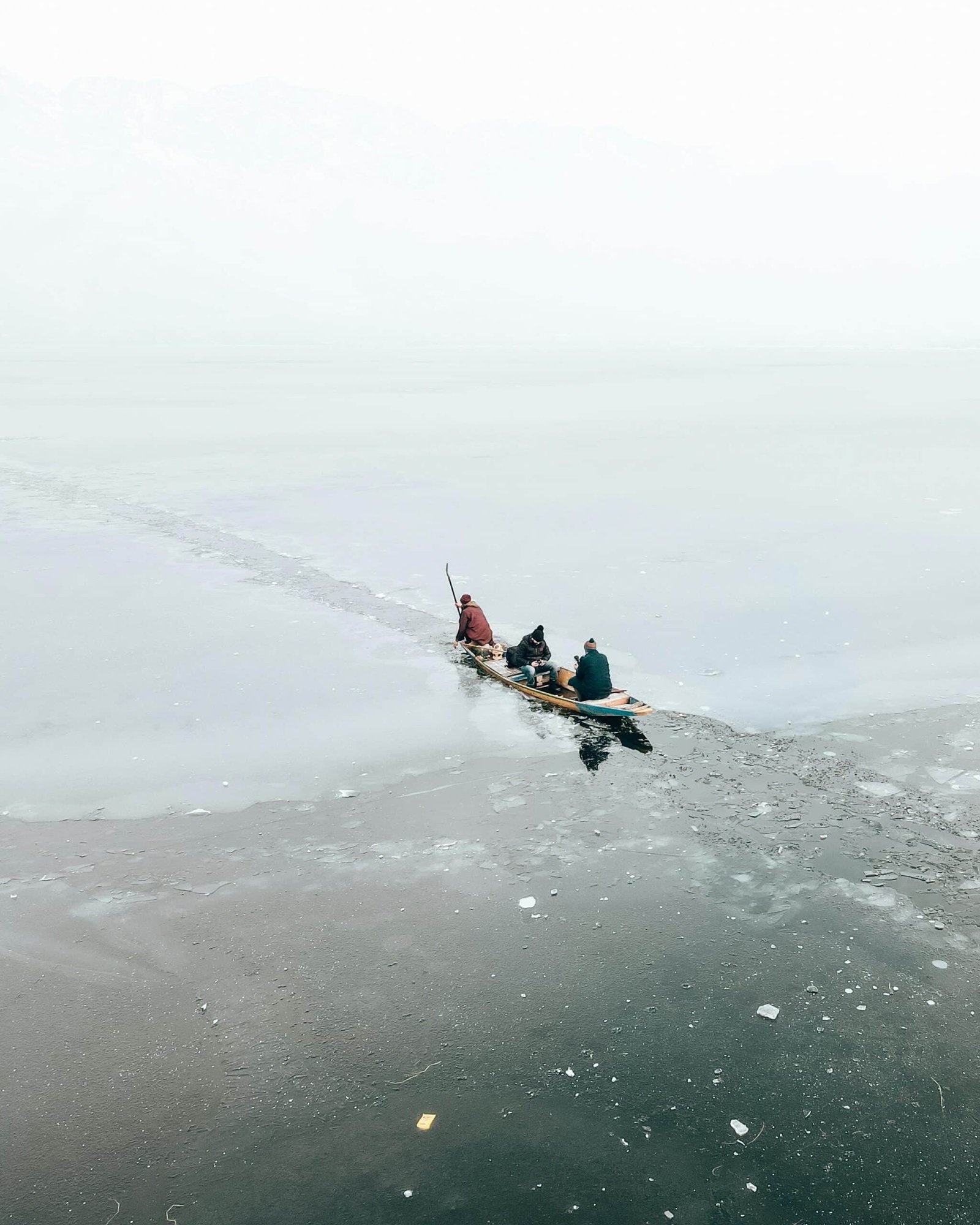 Shikara boat with people gliding through frozen Dal Lake in misty winter weather