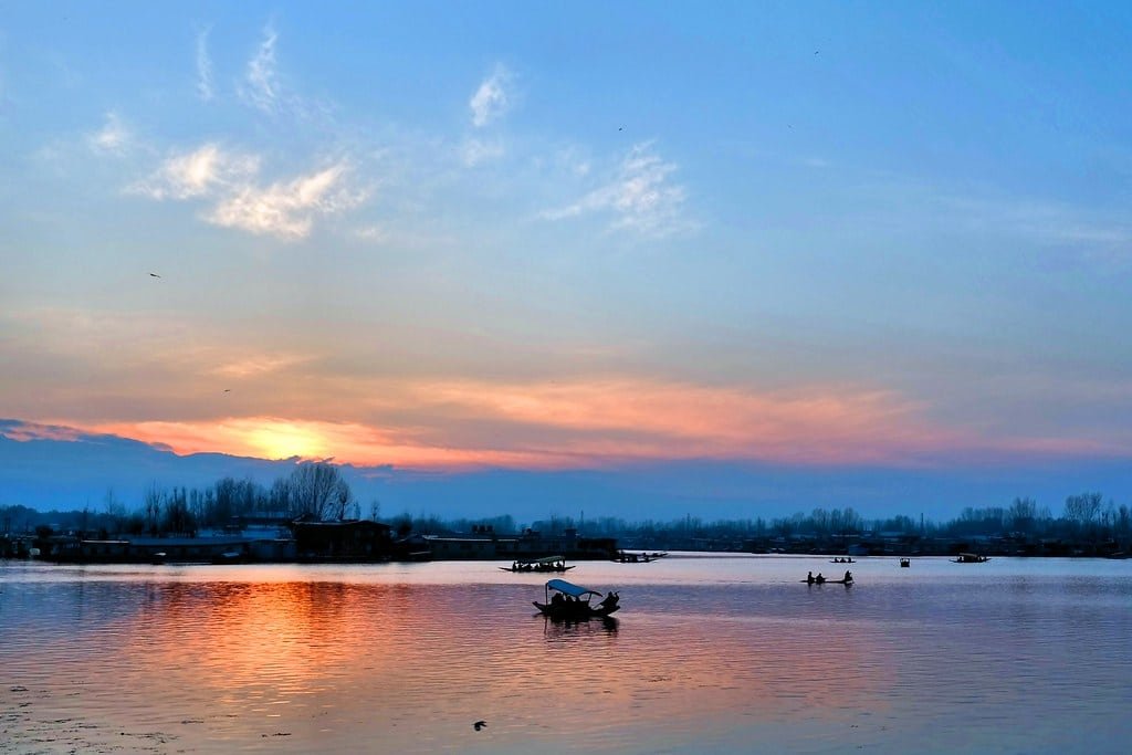 Boats on a calm lake during sunset with colorful reflections in the water.