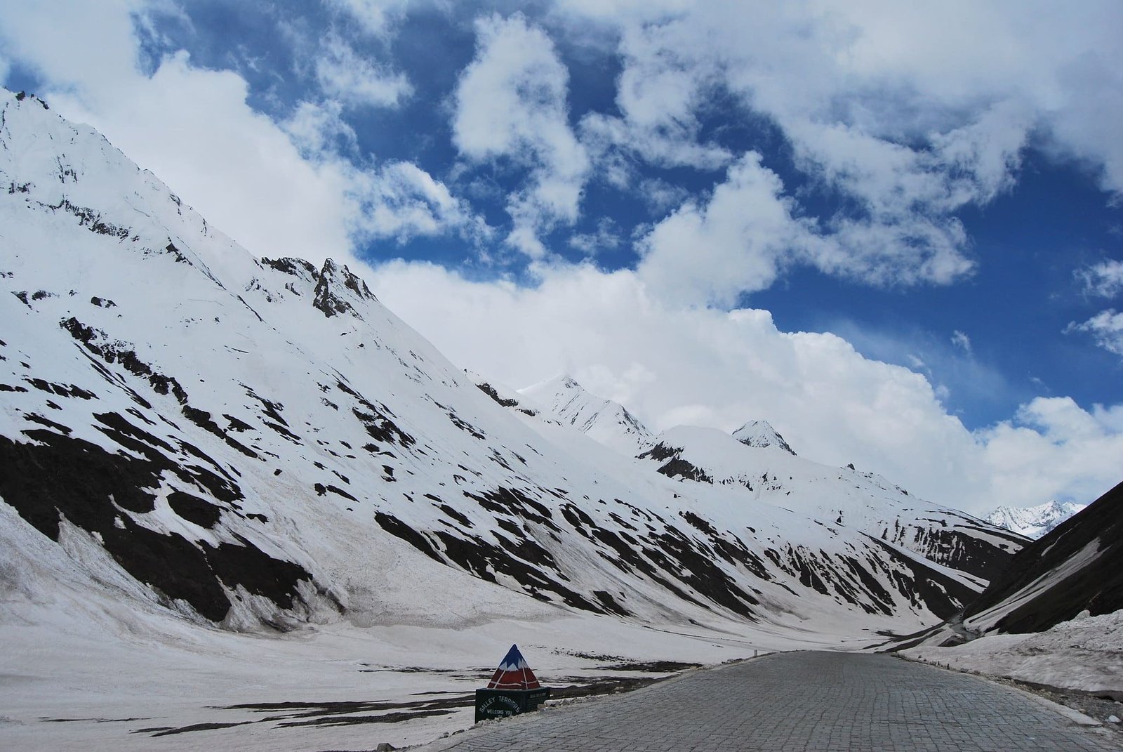 Snow-covered Zoji La Pass with a winding mountain road under a partly cloudy sky