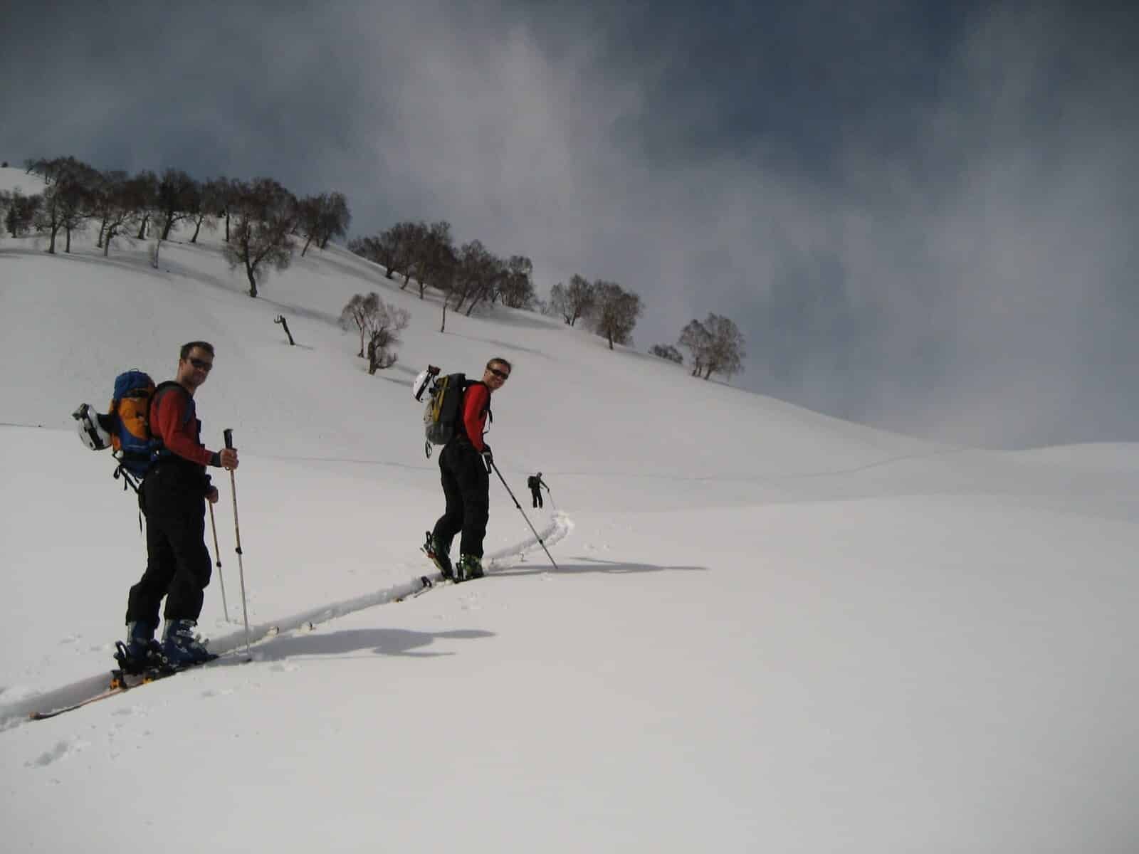 Two backcountry skiers climb a snow-covered slope with poles and backpacks
