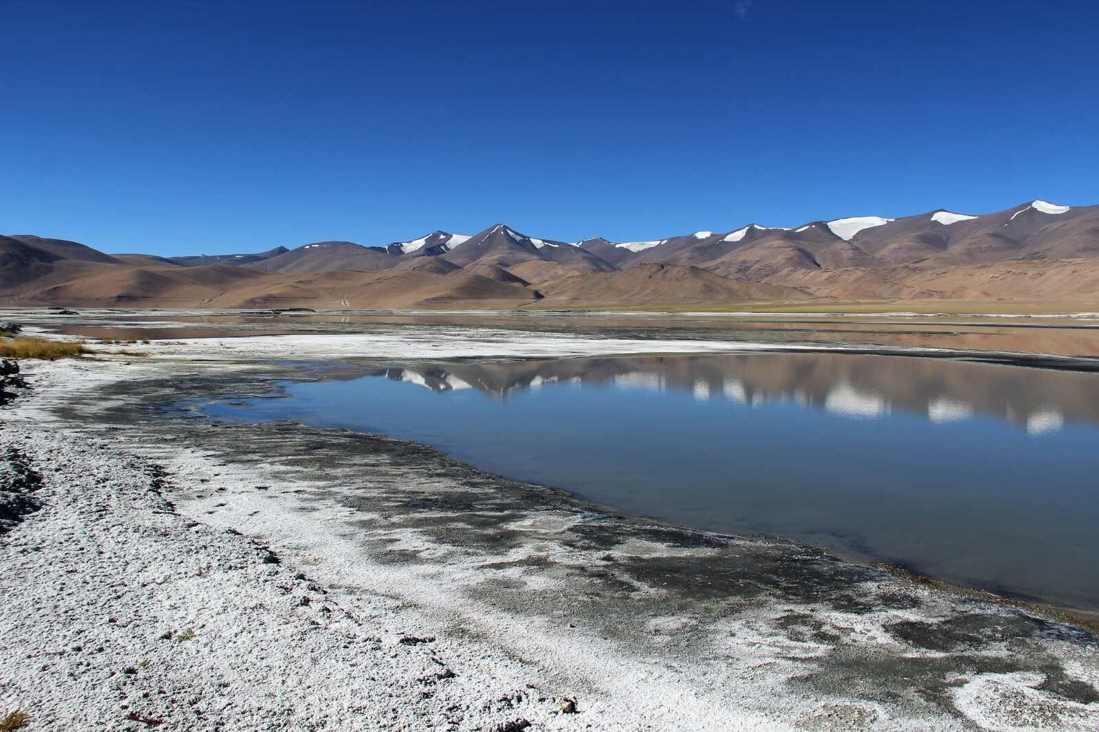 Scenic view of Tso Moriri Lake with snow-dusted shores, calm reflective water, and brown mountains under a clear blue sky