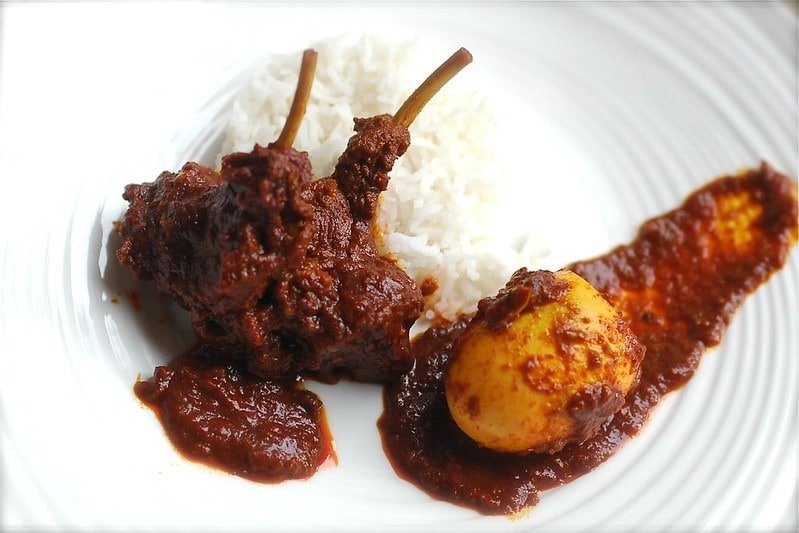 Spicy mutton curry with egg and white rice on a plate.