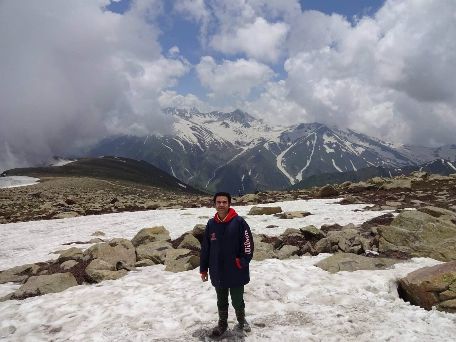 A man stands on a snowy mountain trail with rocky terrain in ladakh