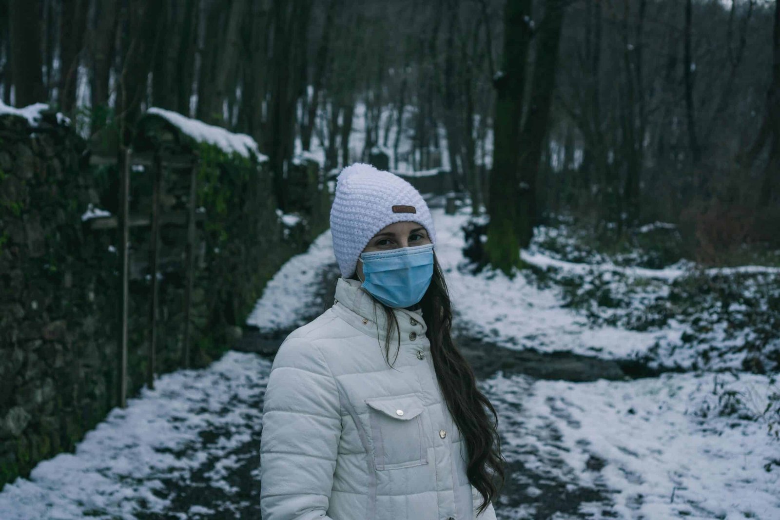 Woman in winter clothes and face mask standing on a snowy forest path in srinagar