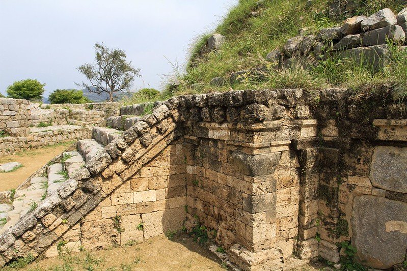 Ancient stone ruins of the Harwan Buddhist Monastery, with weathered steps and moss-covered blocks surrounded by greenery