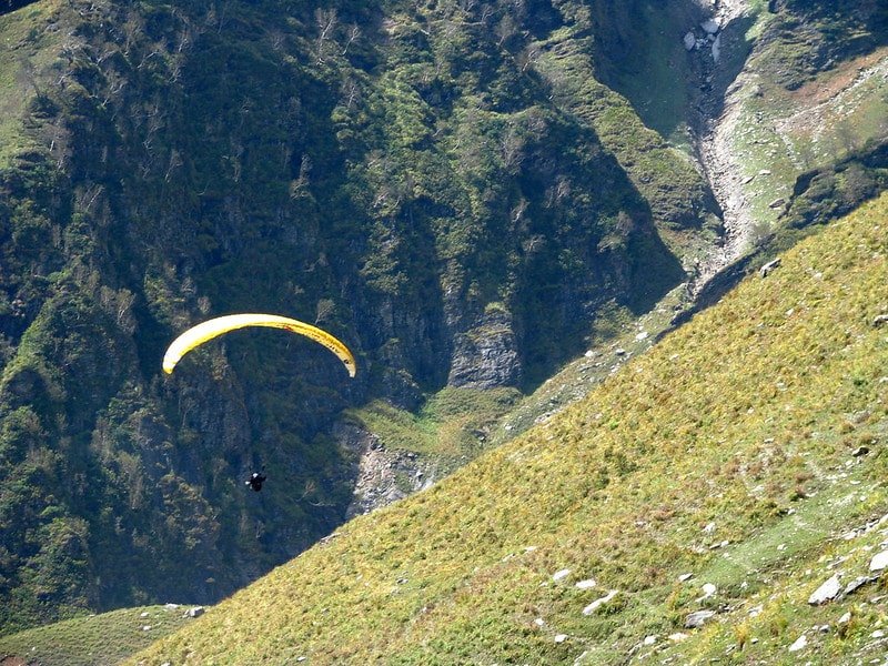 Person paragliding with a yellow parachute over green hills and rocky cliffs in Leh, Ladakh