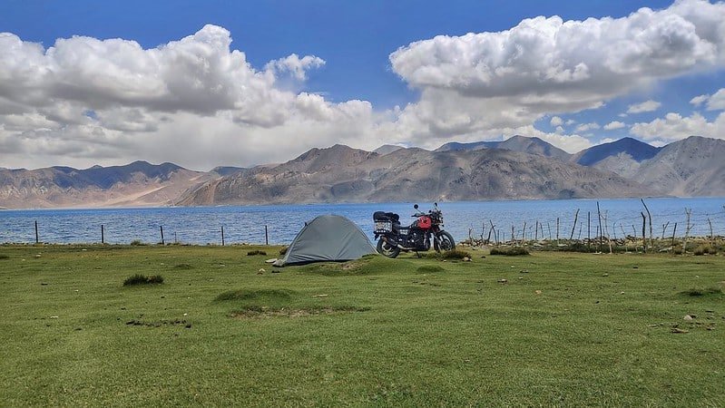 Tent and motorcycle set up on green grass near Pangong Lake, ladakh