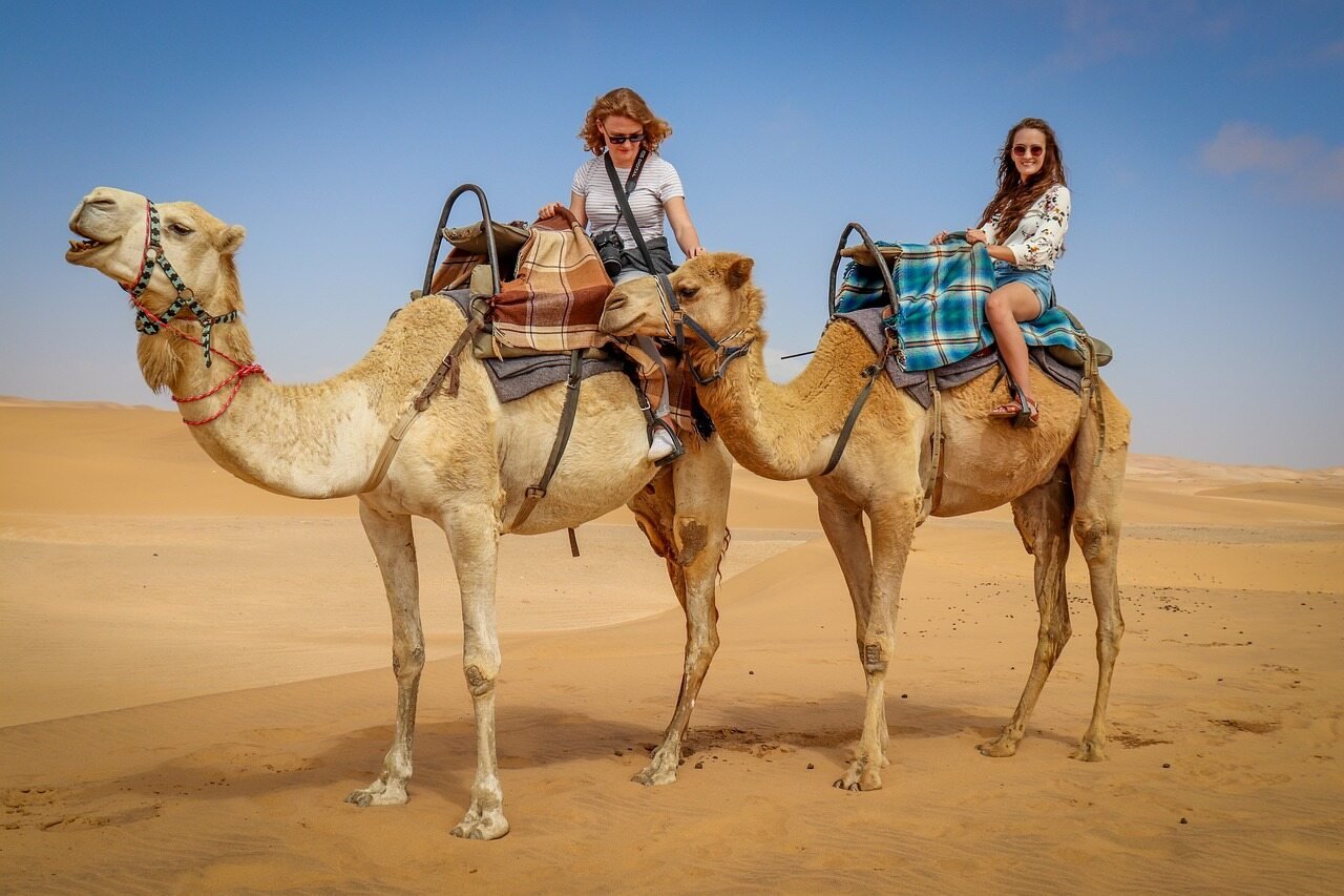 Two women riding camels in the desert.