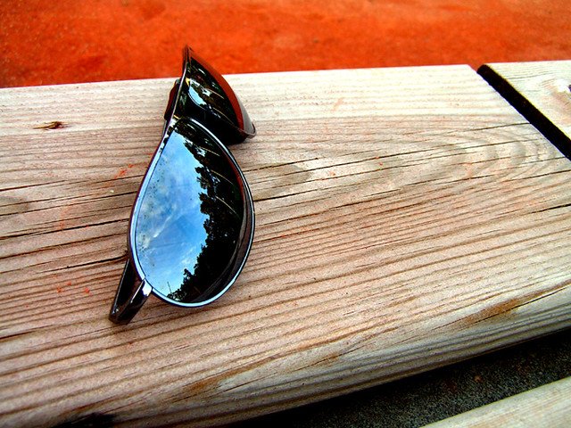 Sunglasses on a wooden bench with sky reflection