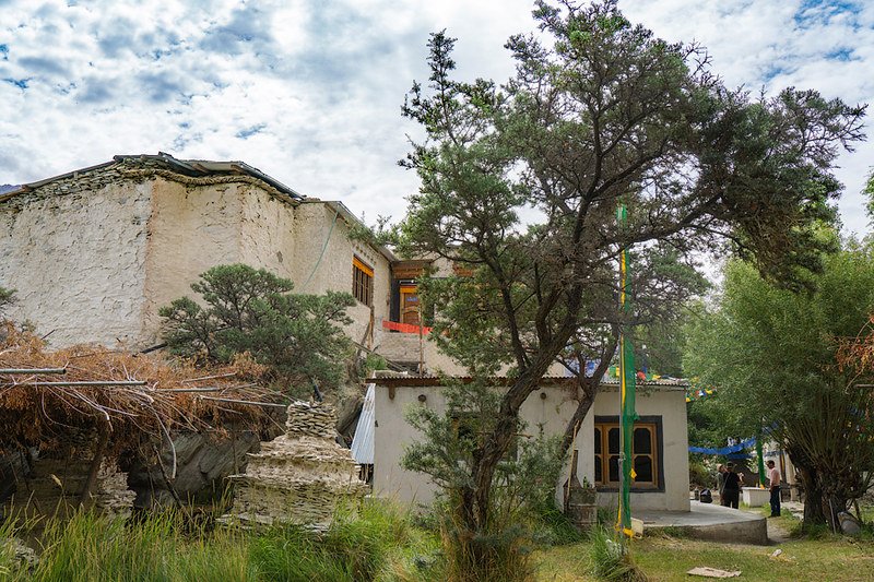 Ensa Gompa surrounded by trees and greenery under a partly cloudy sky