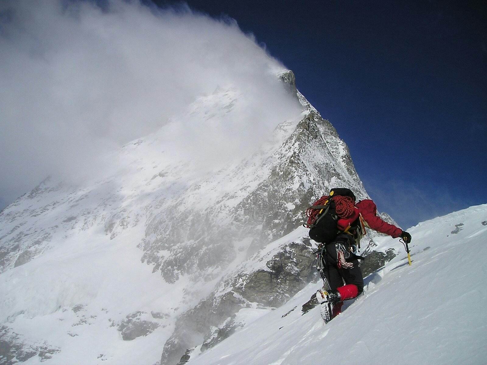 Mountaineer ascending a snowy slope toward a sharp, cloud-covered peak in ladakh